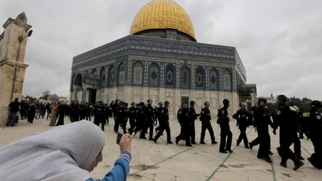 A Palestinian woman takes a picture as Israeli police walk in front of the Dome of the Rock during clashes with stone-throwing protesters after Friday prayers, outside al-Aqsa mosque in the compound known to Muslims as Noble Sanctuary and to Jews as Temple Mount, in Jerusalem's Old City December 6, 2013. Israeli police hurled stun grenades to disperse stone-throwing Palestinian protesters outside the mosque, Islam's third holiest site, after prayers and five people were detained for causing disturbances at the site, a police spokesman said on Friday. REUTERS/Ammar Awad (JERUSALEM - Tags: POLITICS RELIGION CIVIL UNREST) - RTX166NG