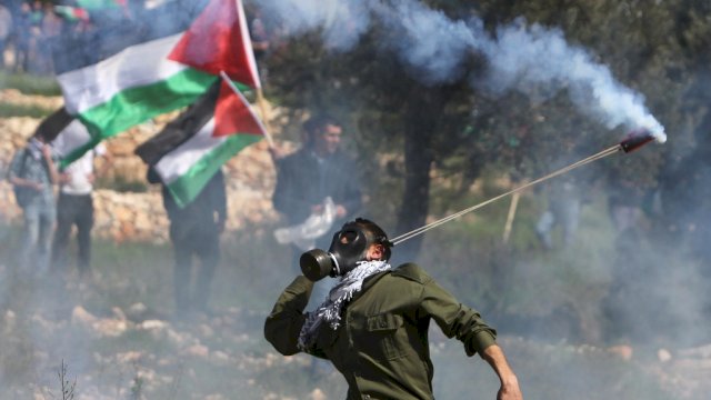 A Palestinian protester throws back a tear gas cannister using a sling shot during clashes with Israeli security forces on February 27, 2015 following a demonstration in the West Bank town of Bilin, near Ramallah, to mark the tenth anniversary of their uprising against the building of Israel's controversial separation barrier and the construction of Israel settlements. AFP PHOTO / ABBAS MOMANI